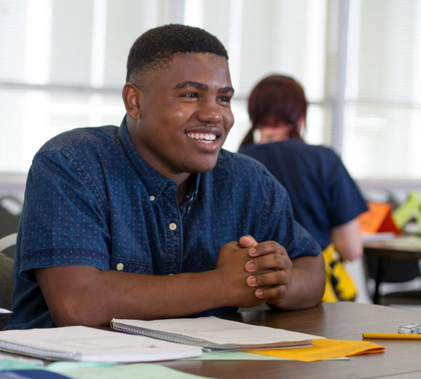 Male student sitting down in class smiling.